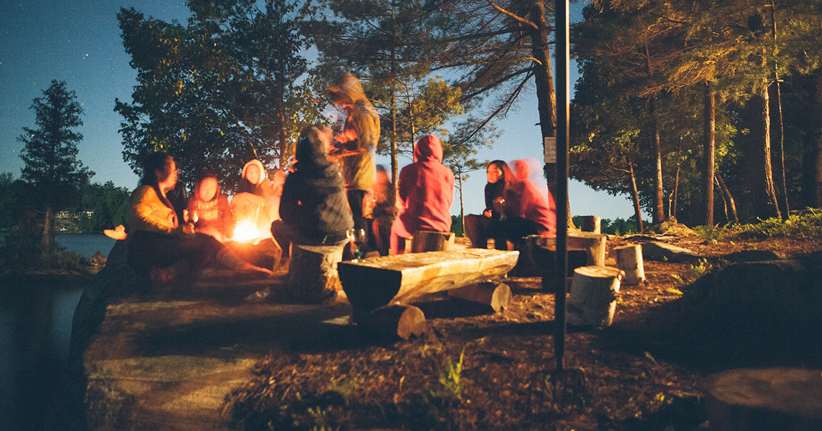 A group of people sitting around a fire in the woods at night