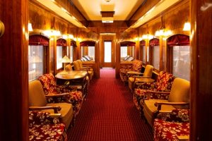 Interior of a restored antique rail car. Red carpet and upholstered chairs below yellow hued lights that light up this old rail car