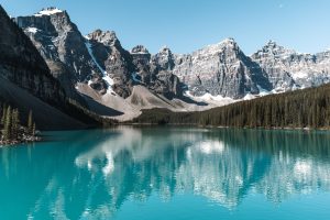 Lake Moraine featuring a turquoise blue lake, framed by a cradle of grey mountains and pine trees