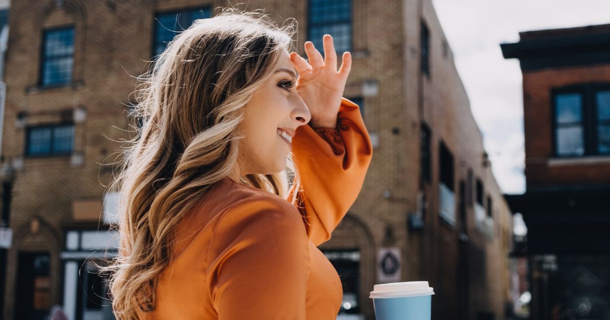 Woman on the street looking into the distance and holding a coffee